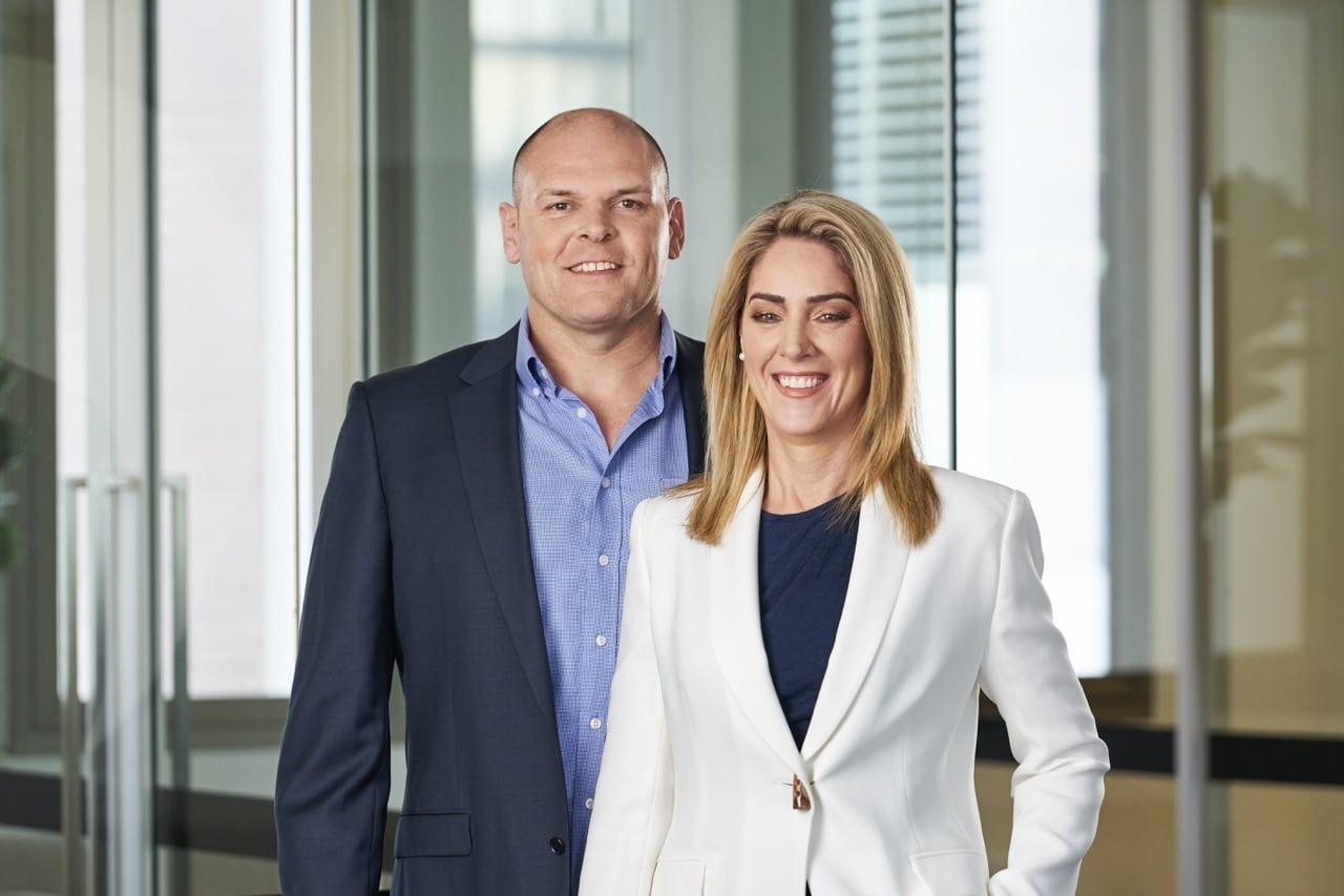 Two professionals smiling in corporate office environment.