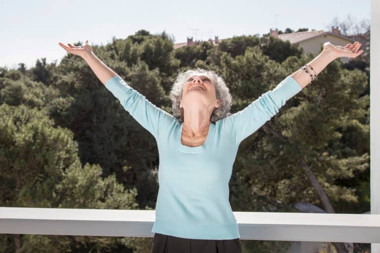 Senior woman enjoying sunshine on balcony.