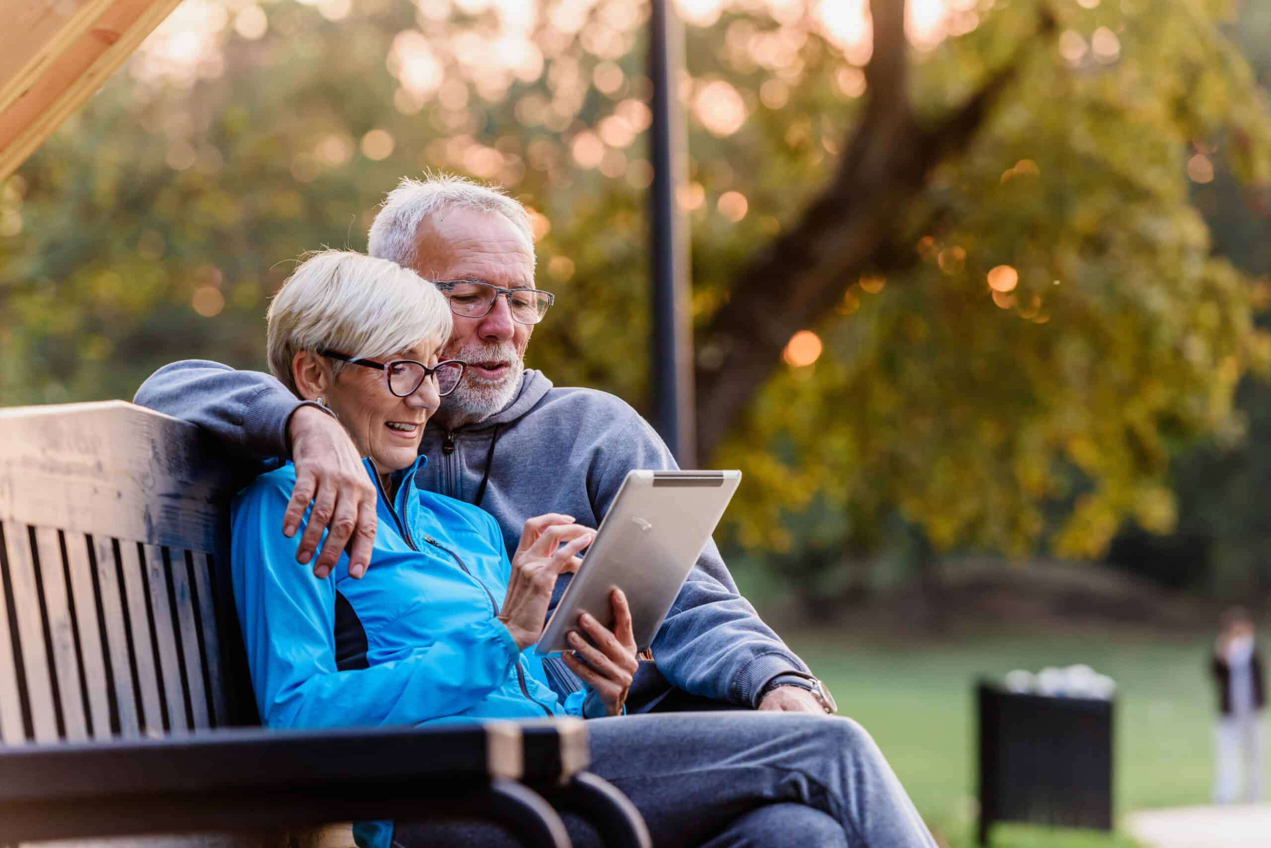 Senior couple using tablet on park bench.