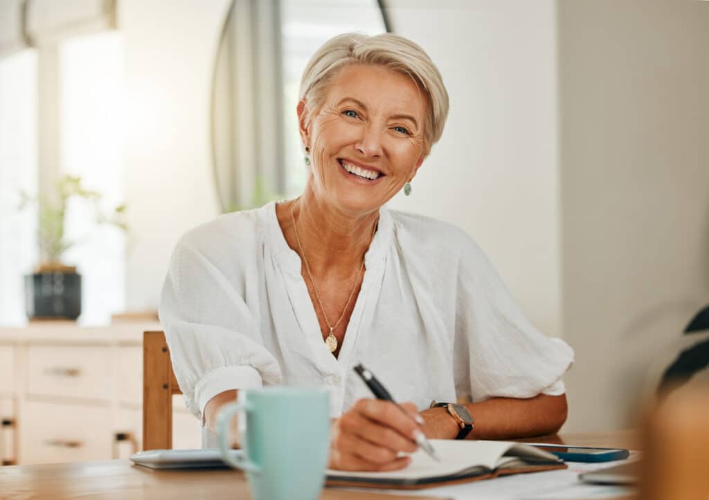 Smiling senior woman writing in notebook at home.