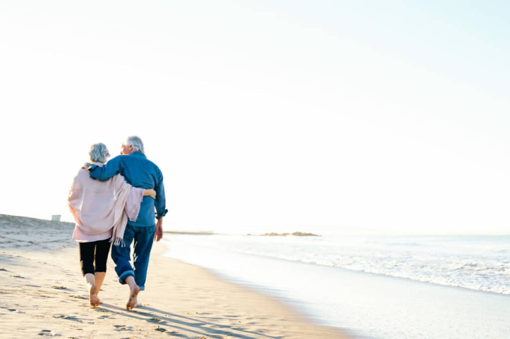 Elderly couple walking on sunlit beach together