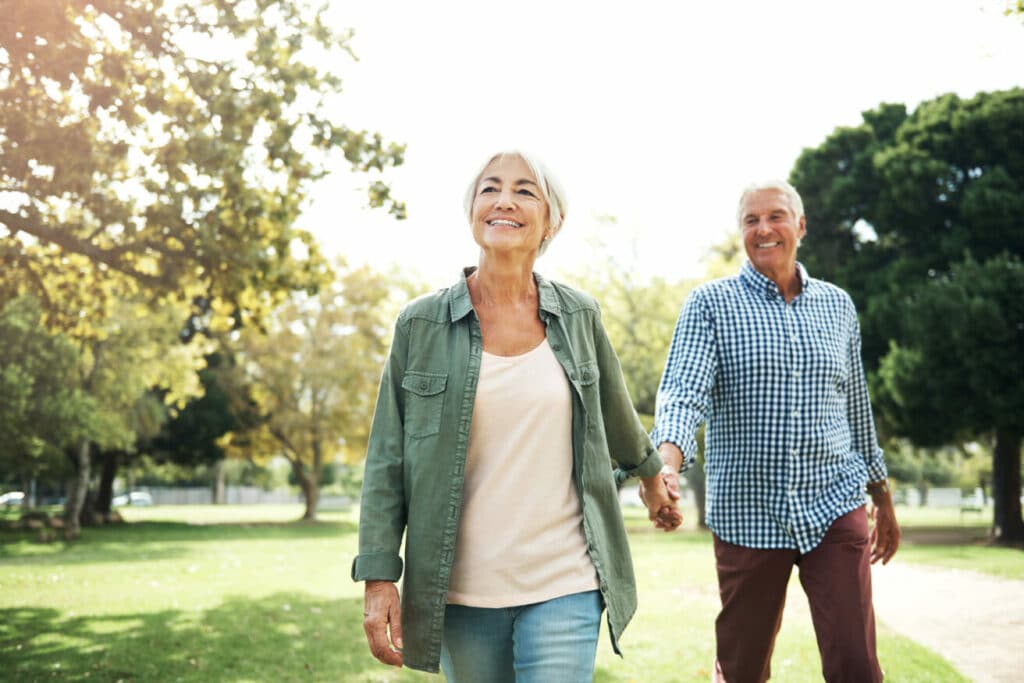 Senior couple walking holding hands in park.