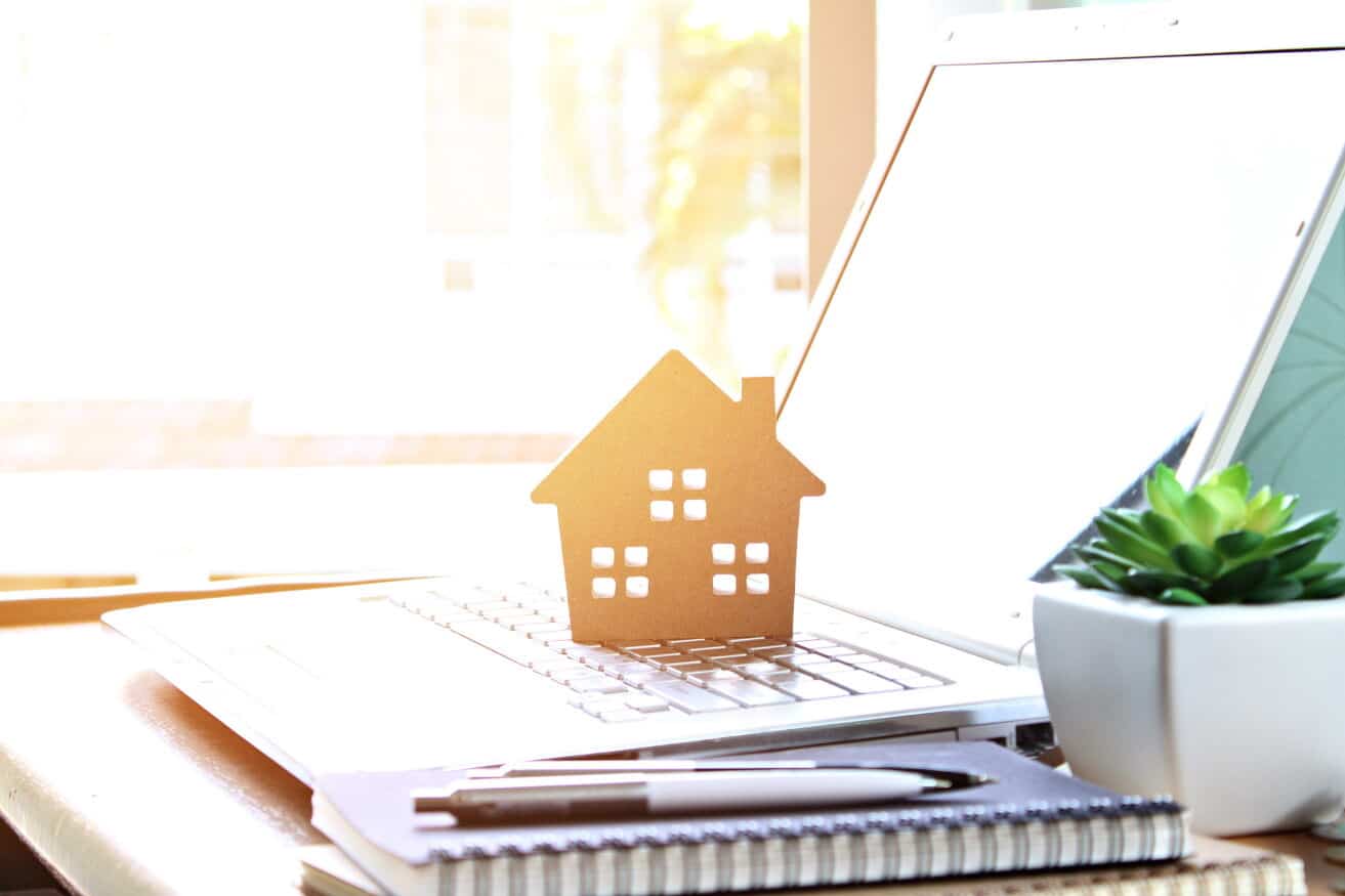 Cardboard house model on laptop, real estate concept.