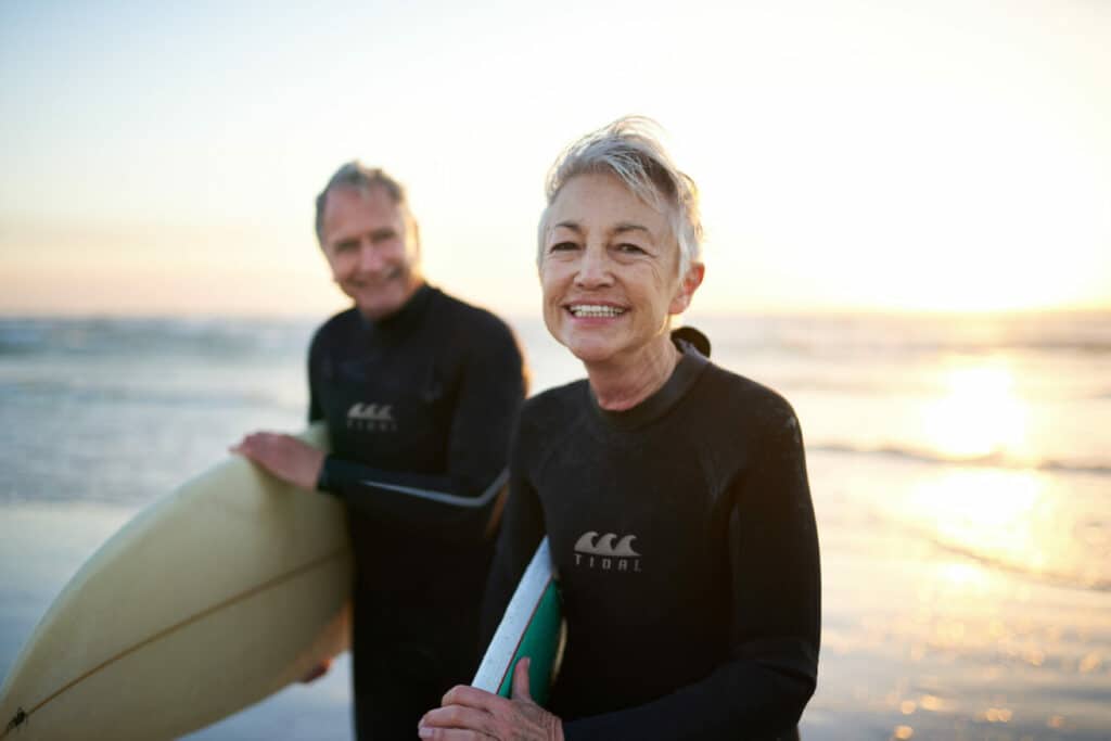 Senior couple with surfboards at sunset on beach