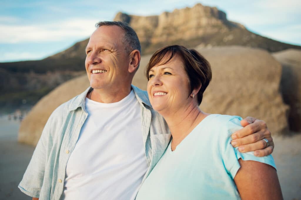 Mature couple smiling together on a beach at sunset.