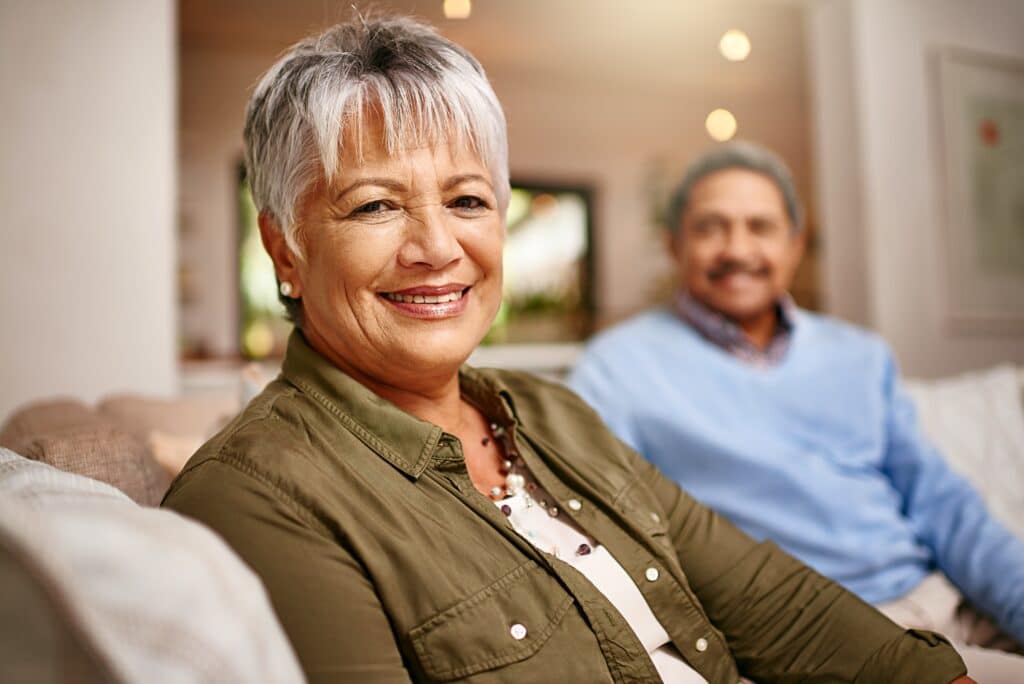 Portrait of a happy older woman relaxing on the sofa with her husband in the background.